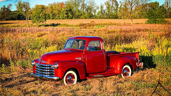 Drone photo of a 1950 Red Chevy 3100 Truck in a field in autumn, by Fox Creek Aerial Productions.