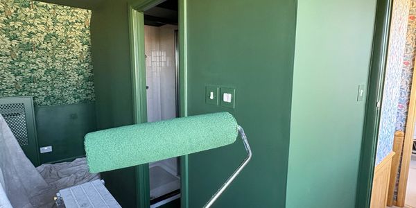A room being painted green with a roller brush in focus.