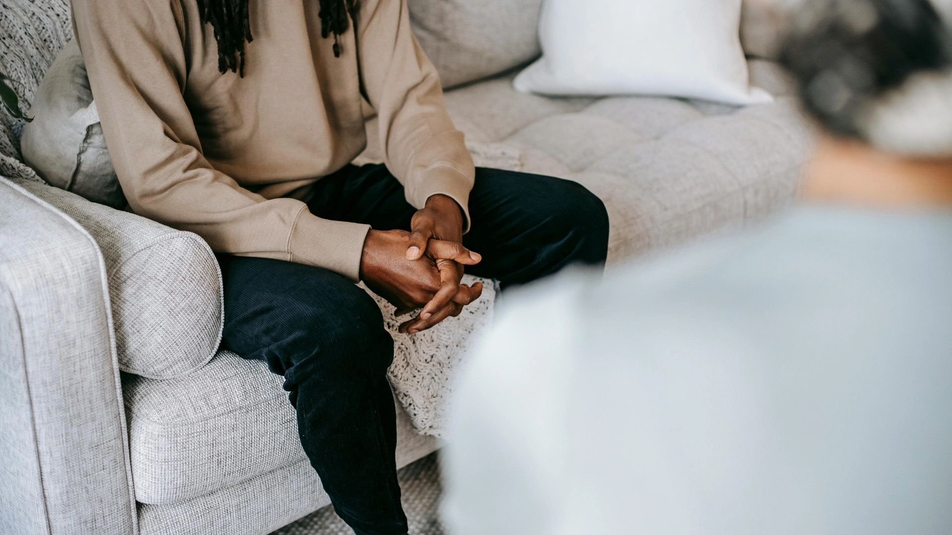 Person sitting with hands clasped on a couch.
