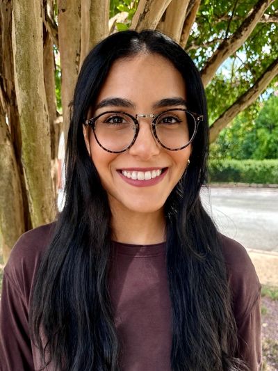 Young woman with glasses smiling outdoors.