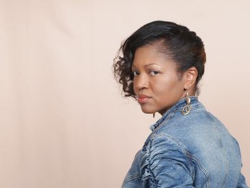 Woman with curly hair in a denim jacket looking over her shoulder.