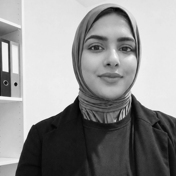 Portrait of a woman wearing a hijab and blazer, smiling softly.