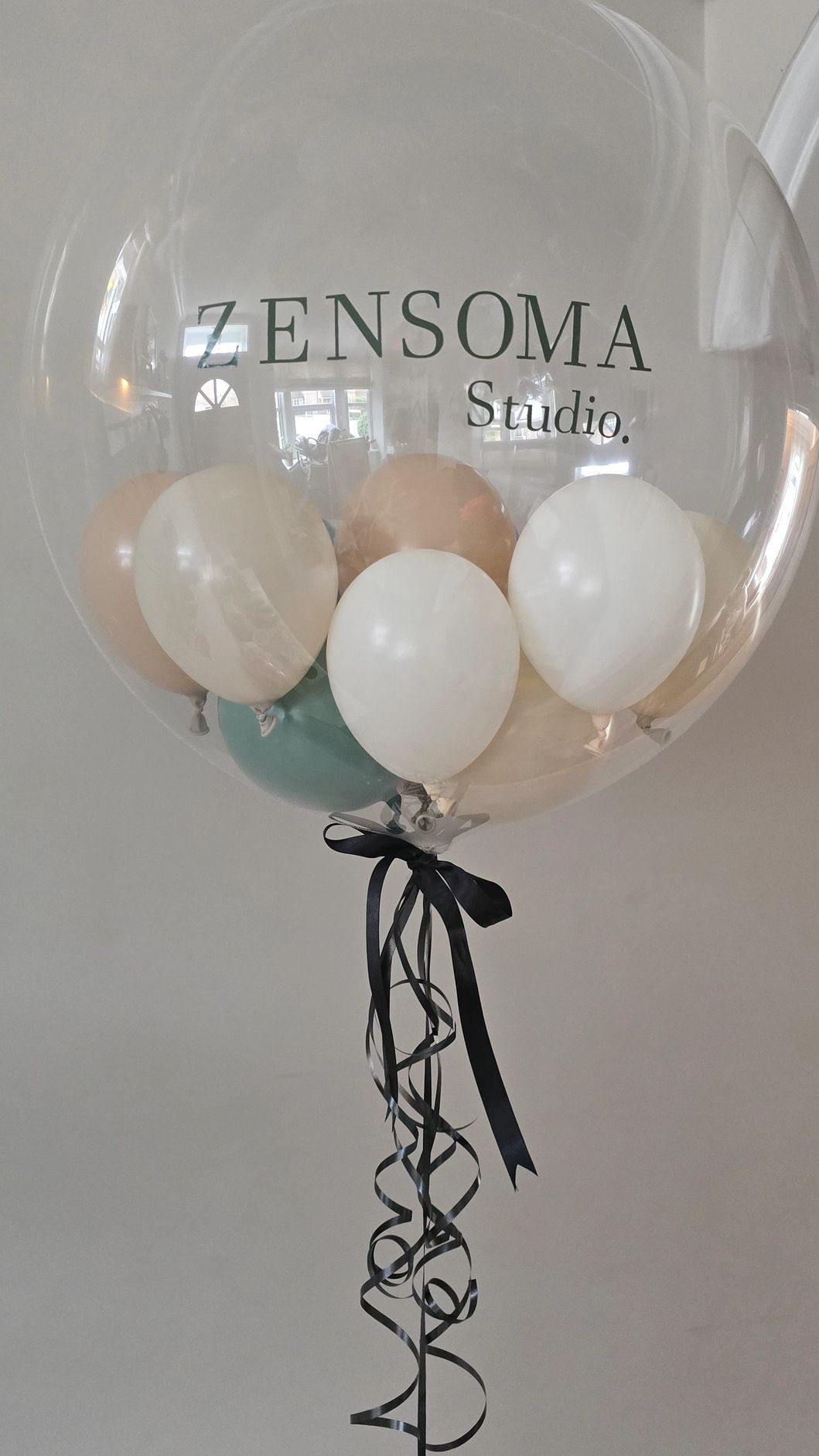 Transparent balloon with smaller pastel balloons inside and black ribbons.