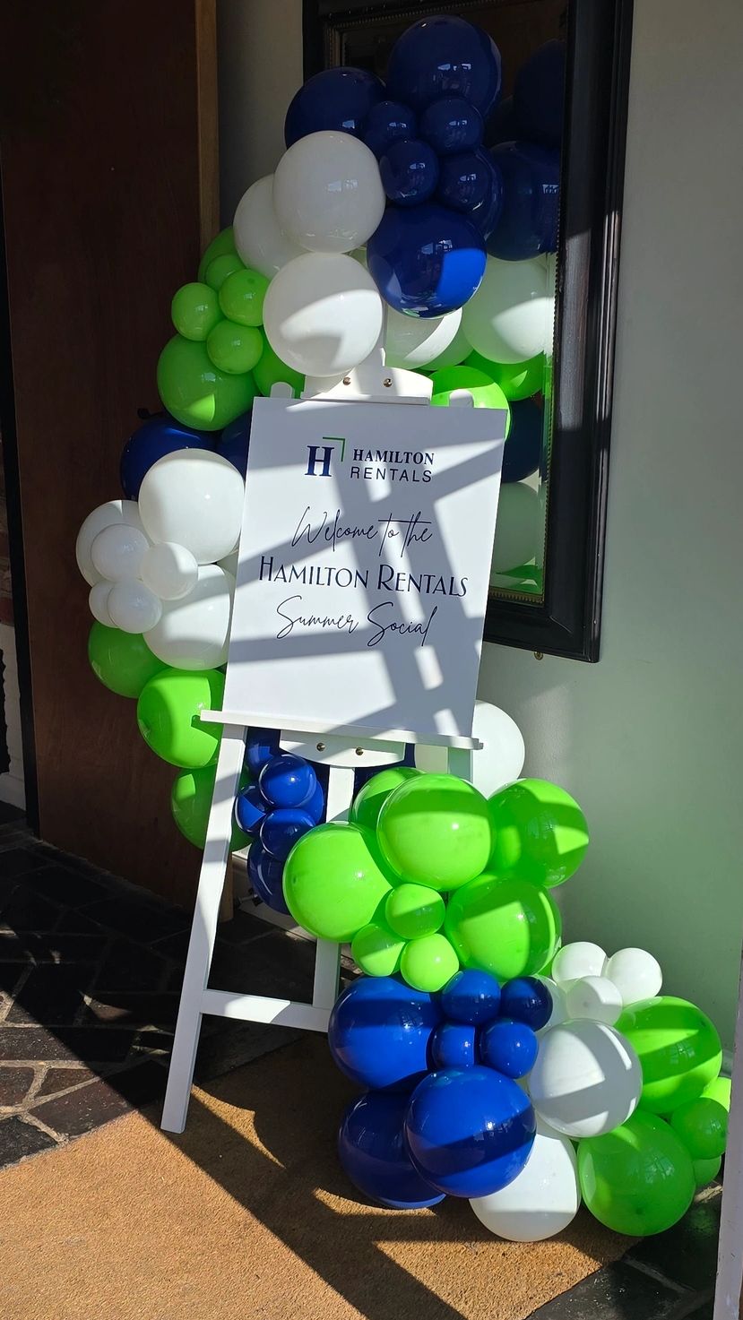 Signboard with colorful balloon decoration welcoming to Hamilton Rentals Social.