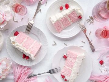 Three slices of pink and white layered cake on plates with raspberries and forks.