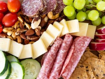 A colorful charcuterie board with meats, cheese, nuts, fruits, and crackers.