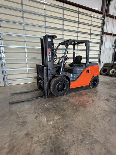 A Toyota forklift parked inside a warehouse with a metal roll-up door.