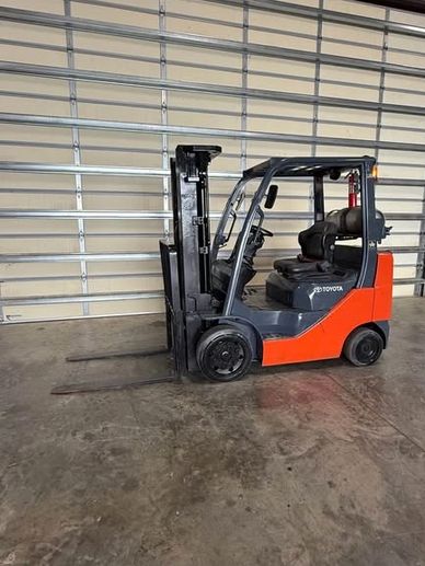 A red and black Toyota forklift parked indoors near a metal door.