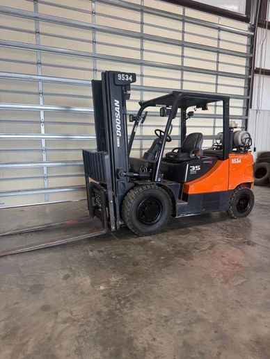 Orange and black Doosan forklift parked indoors on concrete.