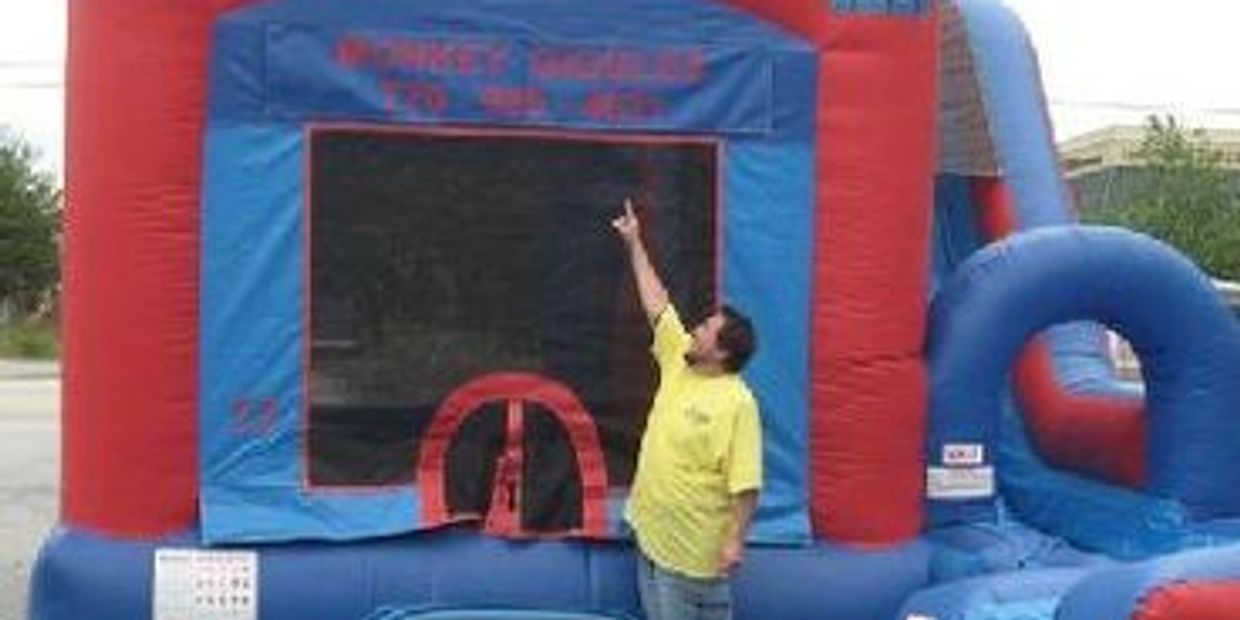 Jump and slide bounce house with person pointing to the banner Monkey Giggles 770-985-4631