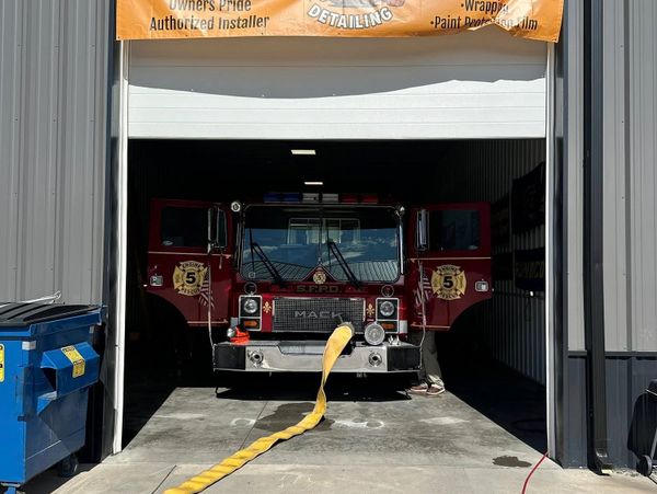 A fire truck with open doors inside a garage and a hose extending out.