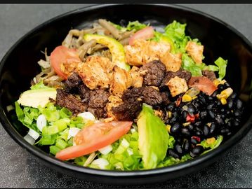Healthy bowl with grilled meats, black beans, and fresh vegetables.