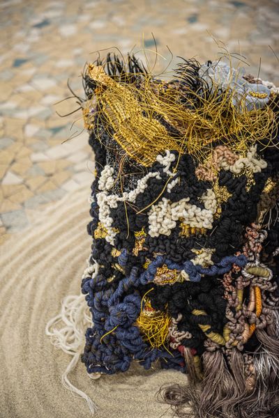 Intricately woven textile art with vibrant threads and textures on a patterned surface.