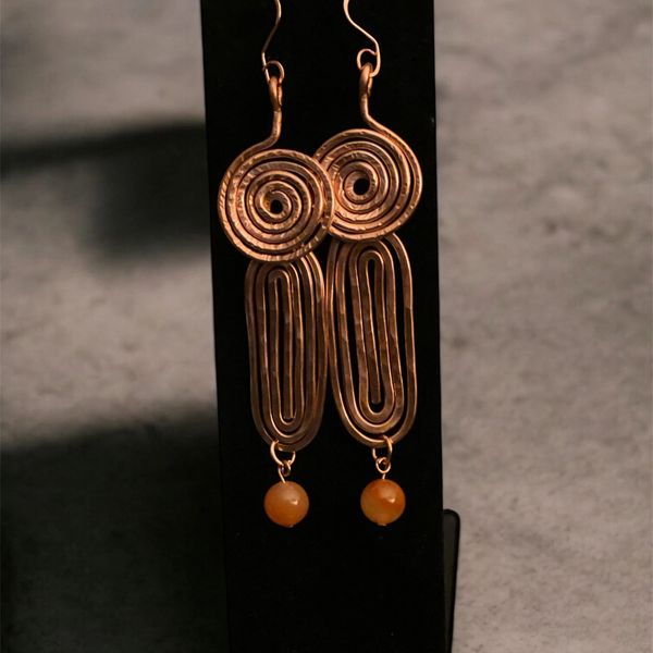 Handcrafted copper earrings with spiral and elongated oval designs, finished with amber beads.