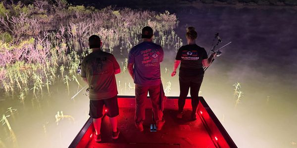 Three people fishing on a boat at night with red lights.