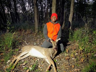 Hunter posing with a deer in the woods.