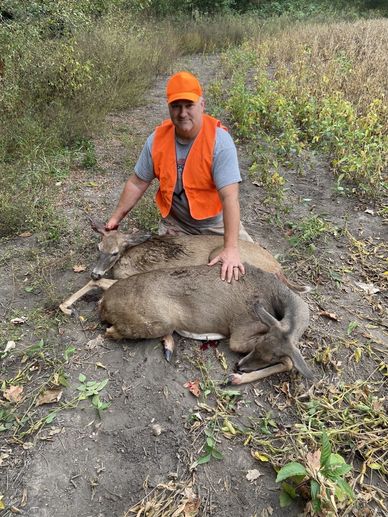 Hunter in orange posing with two deer.