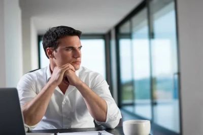 Professional looking out a window in a quiet office setting.