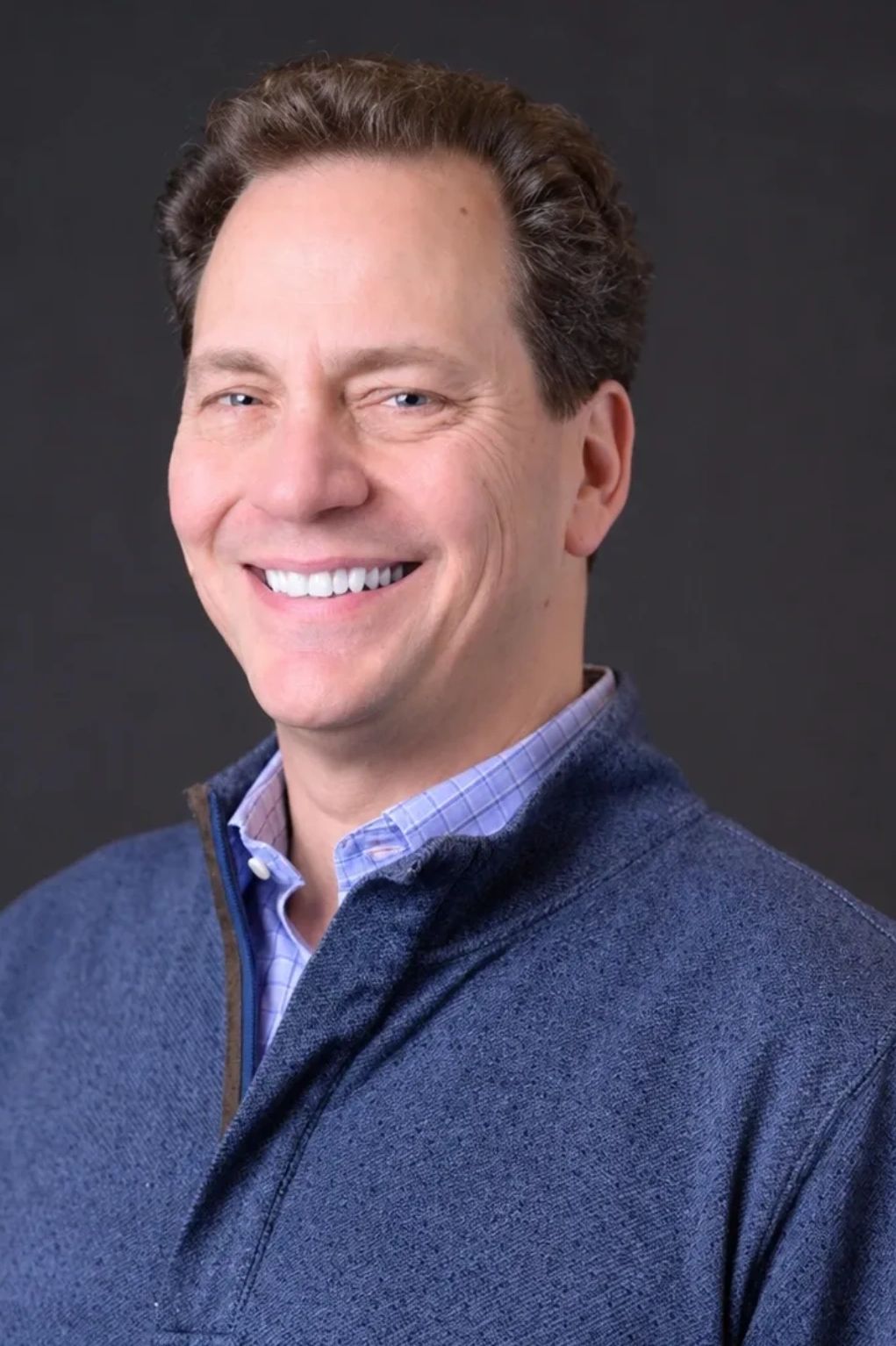 Smiling man in a blue sweater against a dark background.