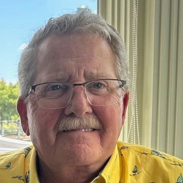 Older man with glasses and yellow shirt smiling.
