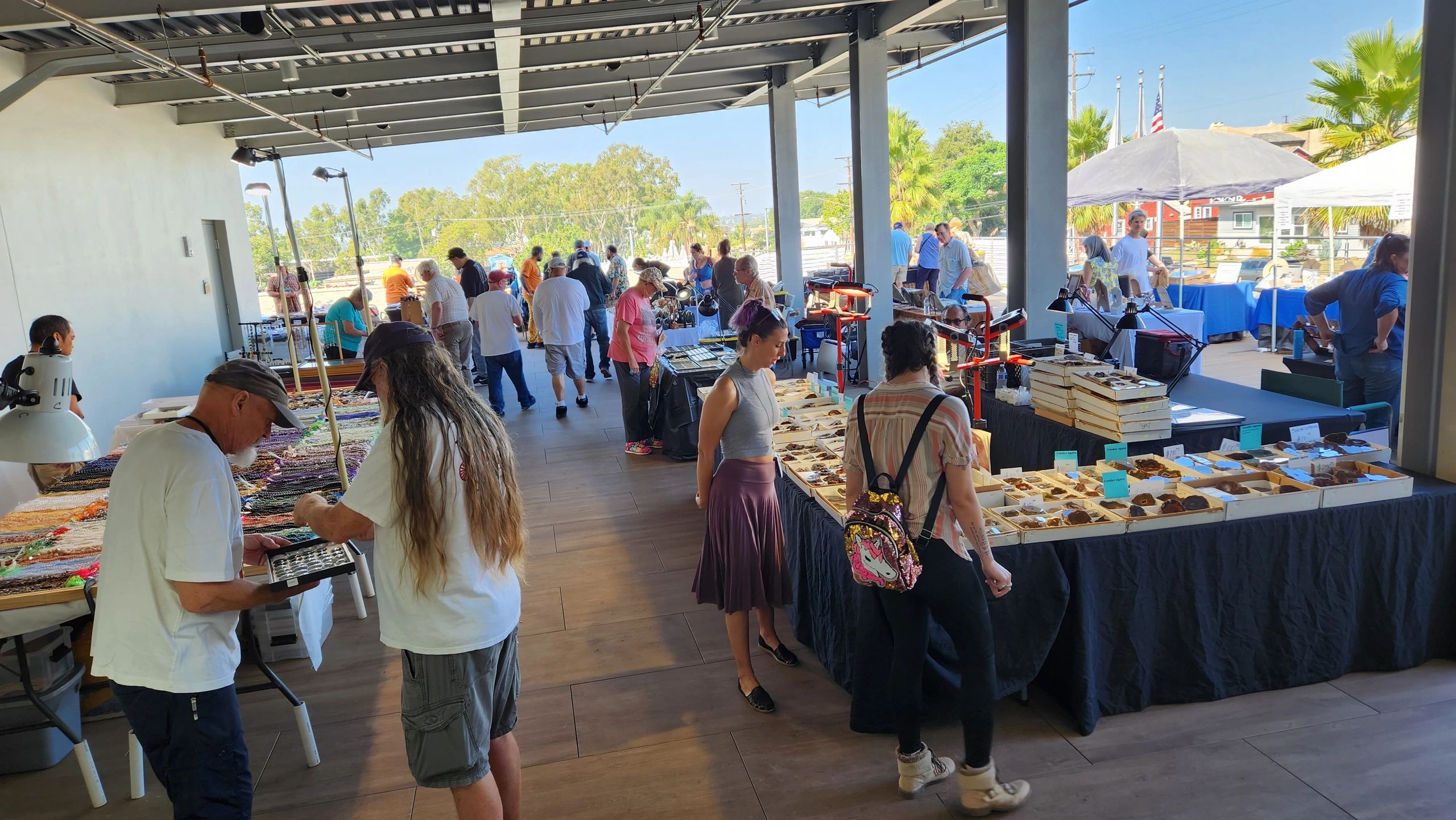 People browsing items at an outdoor market under a covered area.
