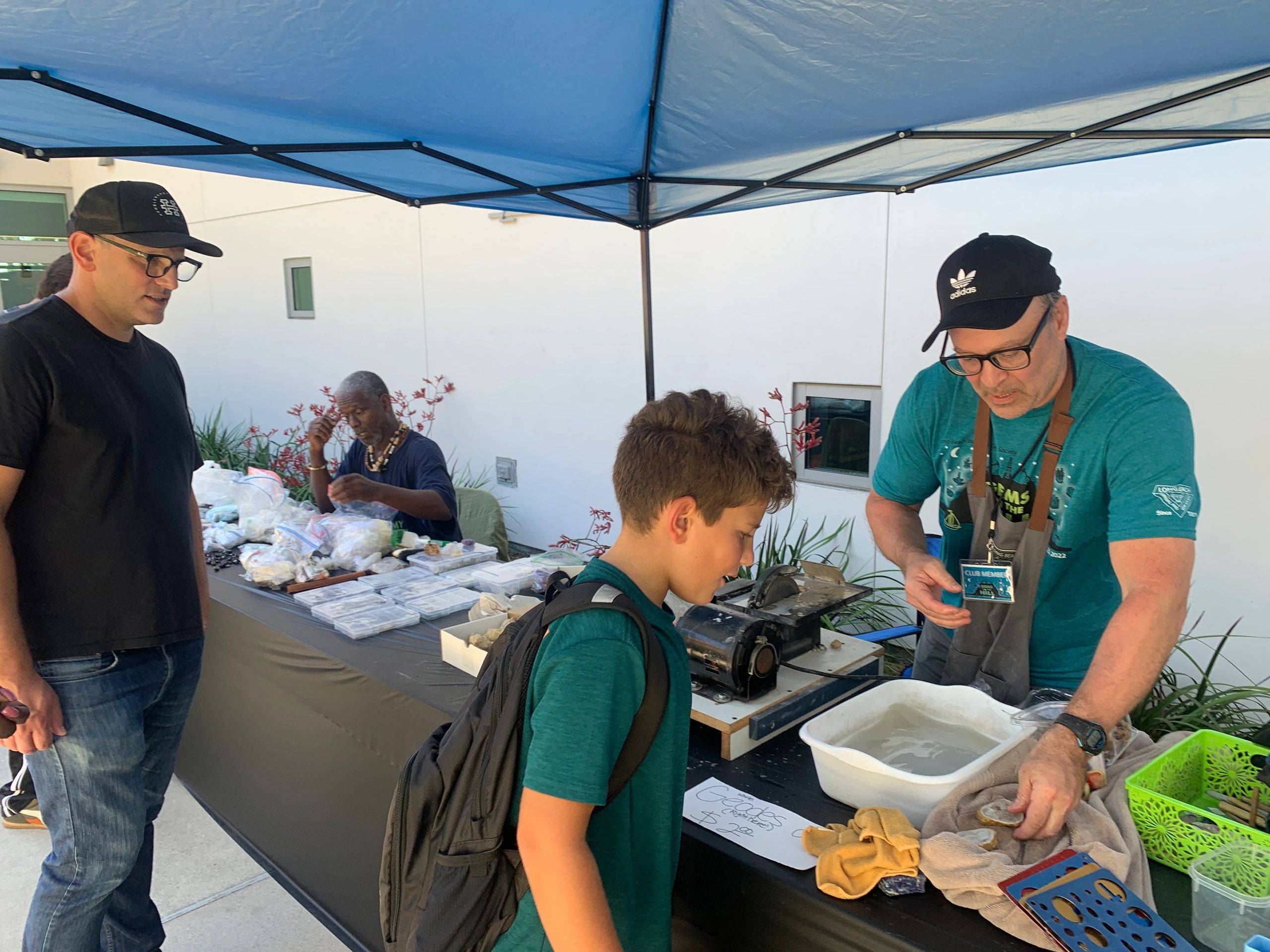 People examining geodes at an outdoor market under a blue canopy.
