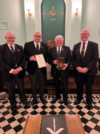 Four men in formal attire stand in a ceremonial room with Masonic symbols.