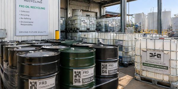 Industrial site with barrels labeled 'FR3 Dielectric Fluid' for oil recycling.