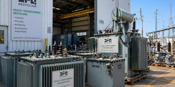Industrial transformers at a recycling facility under a clear sky.