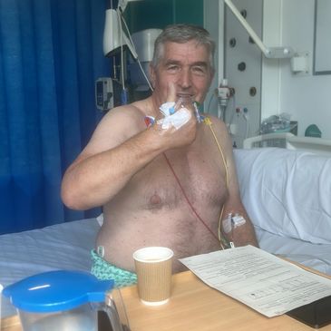 Man giving thumbs up in hospital bed.