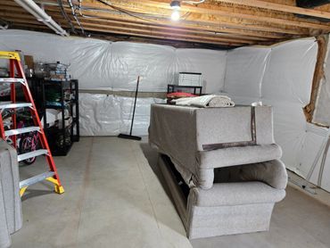 A basement with a sofa, ladder, and shelves, under construction or renovation.