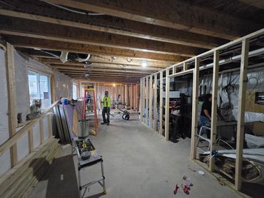 Basement under construction with exposed wooden framing and workers inside.