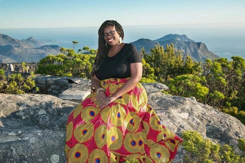 Woman in vibrant skirt smiling atop rocky mountain scenery.