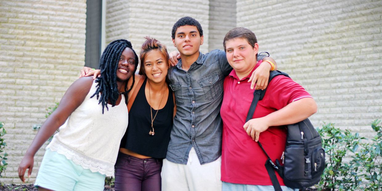 Four diverse friends smiling and posing together outside by a brick wall.