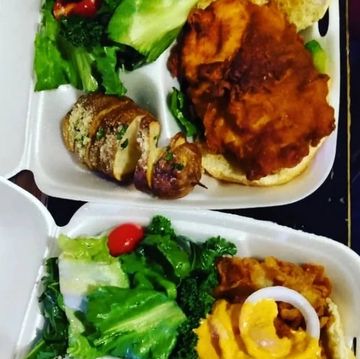 Two takeout containers with fried chicken, salad, and baked potato slices.