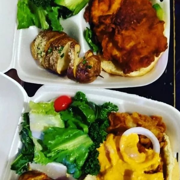 Two takeout containers with fried chicken sandwiches and fresh salads.
