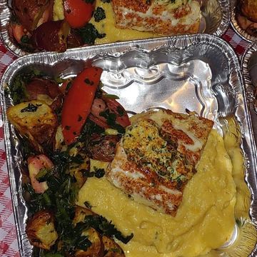 Grilled fish with mashed potatoes and sautéed vegetables in a foil container.