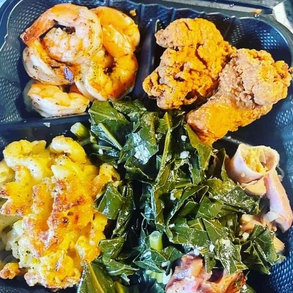 A meal with fried shrimp, fried chicken, mac and cheese, and cooked greens in a black container.