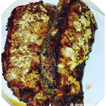 Two grilled steaks topped with chopped garlic on a white plate.