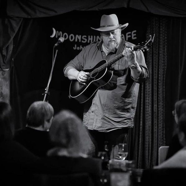 Man in hat playing guitar on stage at Moonshine Cafe.