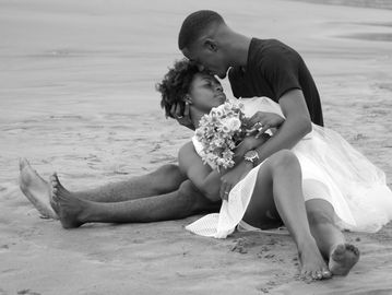 Couple sharing a tender moment on the sandy beach, with the woman holding a bouquet.