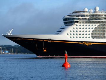 The bow of the Disney Dream cruise ship docks near a red buoy in calm waters.