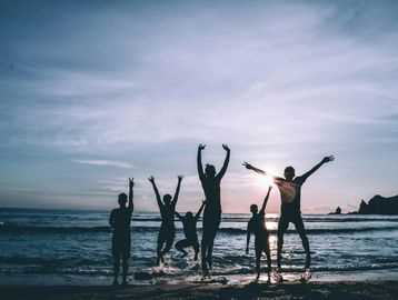 Silhouettes of six people joyfully jumping on a beach at sunset.
