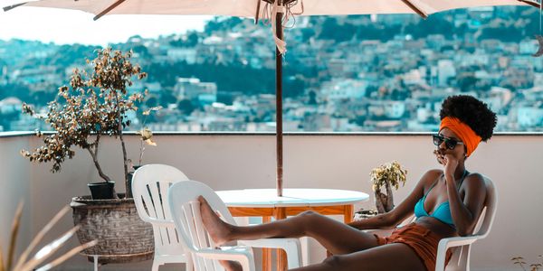 Woman relaxing on a terrace under an umbrella with a cityscape view.