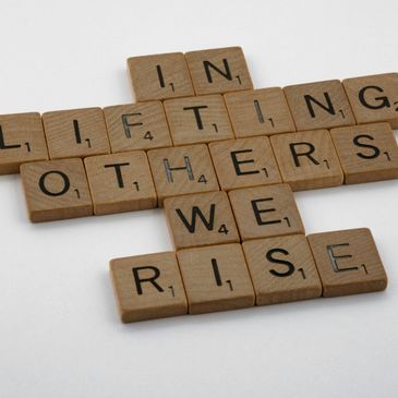 Scrabble tiles forming the phrase 'In lifting others we rise'.