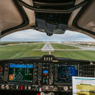 Pilot's view of an aircraft cockpit approaching a runway for landing.