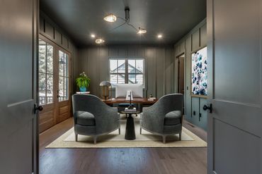 Modern home office with dark walls and cozy seating area.