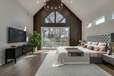 Modern bedroom with vaulted ceiling, large windows, and cozy bed setup.
