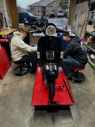 Two people working on a scooter in a garage.