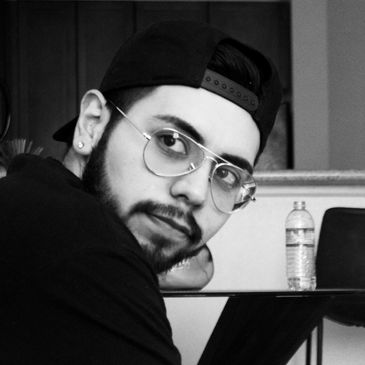 Young man wearing glasses and a backward cap, looking over his shoulder.